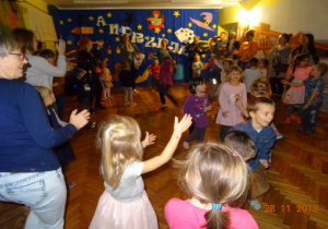 Dzieci oraz rodzice wspólnie tańczą na tle dekoracji.